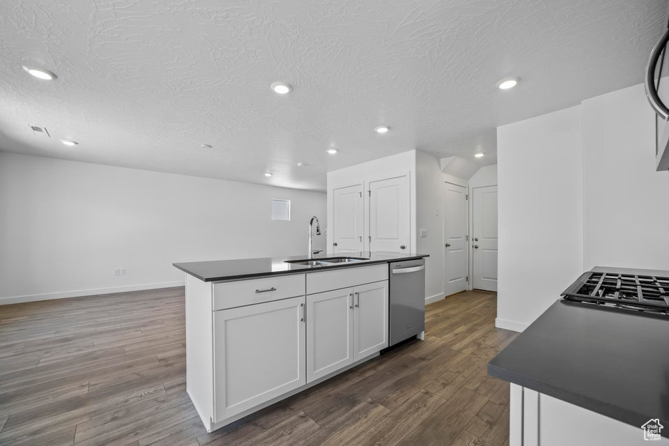 Kitchen with dark countertops, stainless steel dishwasher, recessed lighting, dark wood-style floors, and white cabinets
