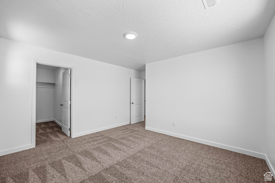 Unfurnished bedroom with carpet floors, a spacious closet, and a textured ceiling