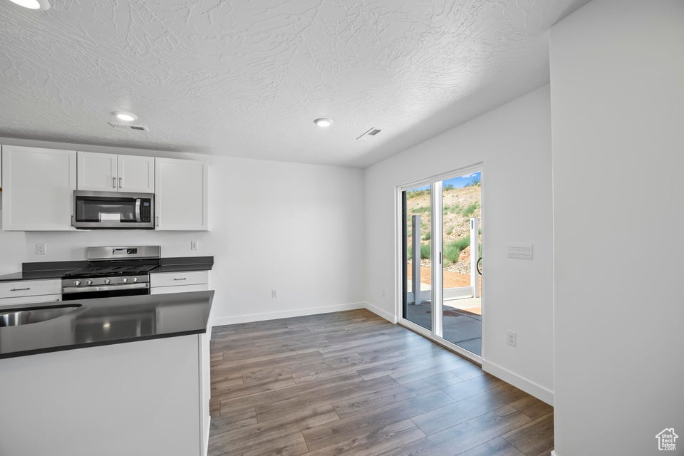 Kitchen with stainless steel appliances, dark countertops, wood finished floors, white cabinets, and recessed lighting