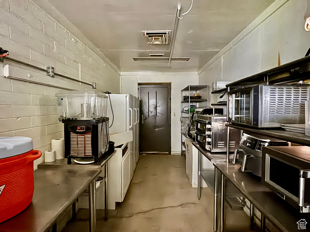 Kitchen featuring finished concrete flooring, concrete block wall, stainless steel microwave, and dark countertops