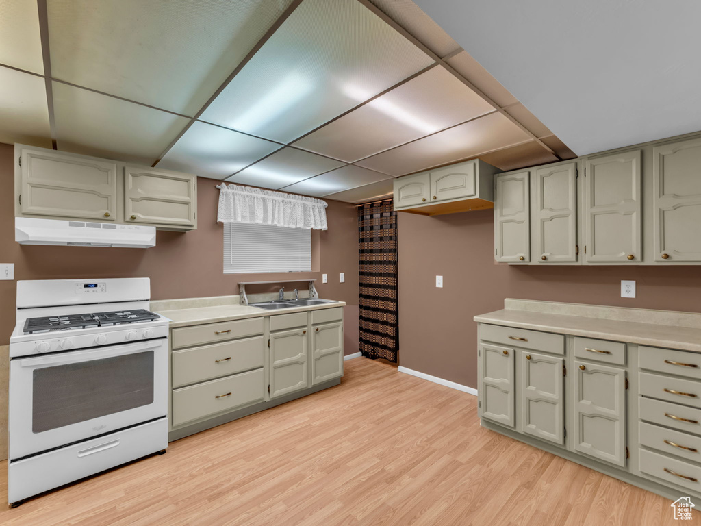 Kitchen featuring white gas range, under cabinet range hood, light wood-style flooring, a paneled ceiling, and light countertops