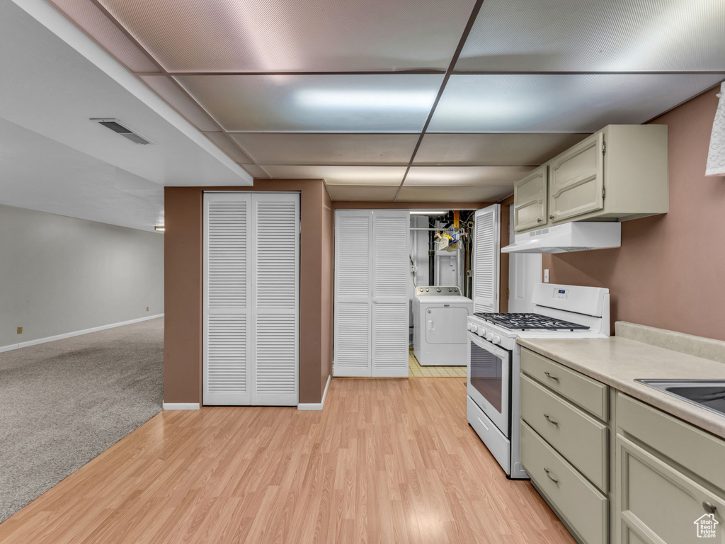 Kitchen featuring white gas stove, washer / dryer, under cabinet range hood, light countertops, and light wood-style flooring