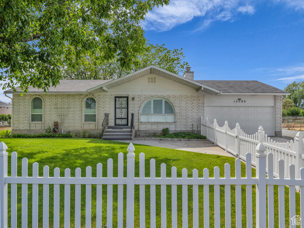 Ranch-style home with a fenced front yard, an attached garage, a chimney, and concrete driveway
