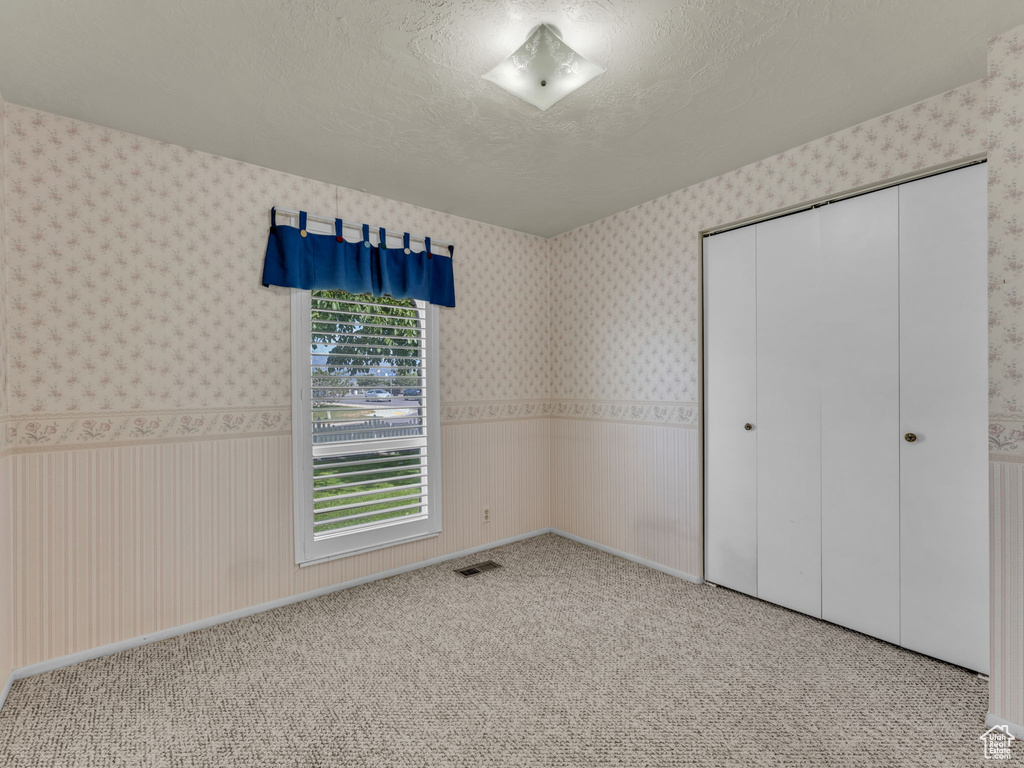 Unfurnished bedroom featuring wallpapered walls, a closet, carpet, and a textured ceiling
