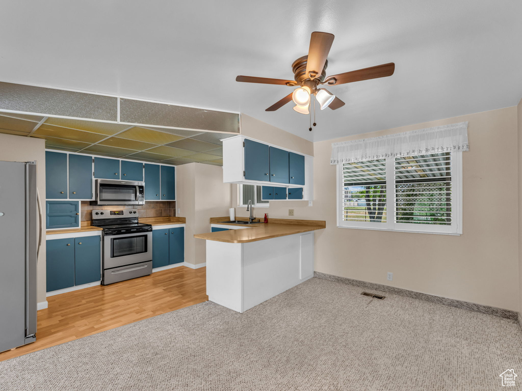 Kitchen with stainless steel appliances, blue cabinets, light carpet, a ceiling fan, and a peninsula