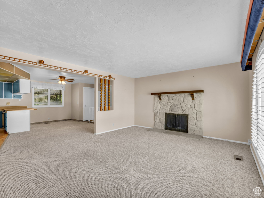Unfurnished living room featuring a stone fireplace, a ceiling fan, carpet floors, and a textured ceiling