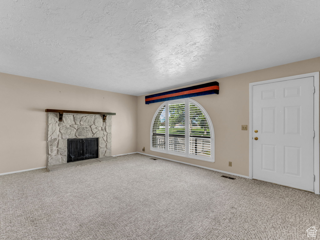 Unfurnished living room with a textured ceiling, carpet, and a fireplace
