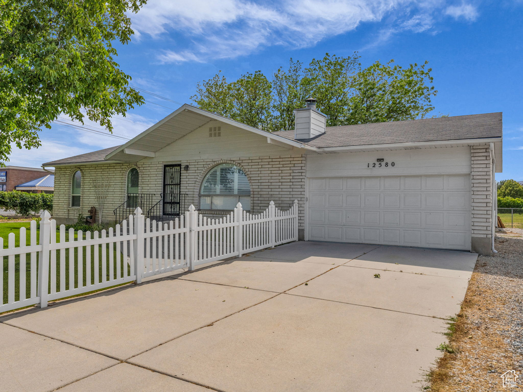 Single story home with a garage, brick siding, driveway, a fenced front yard, and a chimney