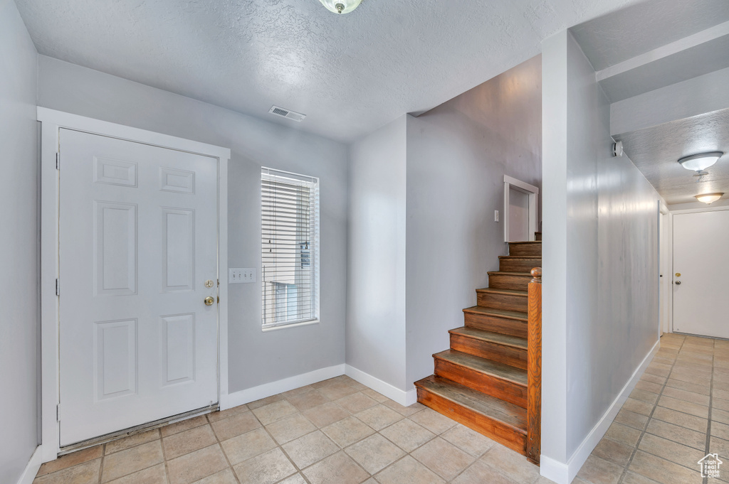 Foyer entrance with a textured ceiling, light tile patterned floors, and stairs
