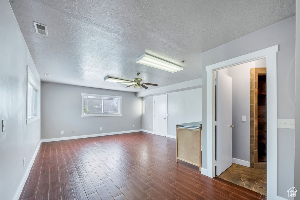 Empty room with a textured ceiling, ceiling fan, and dark wood-style flooring