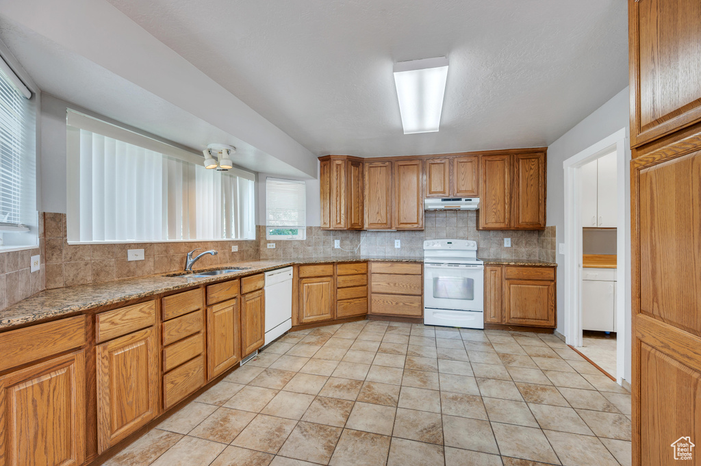 Kitchen featuring white appliances, under cabinet range hood, decorative backsplash, and light stone counters