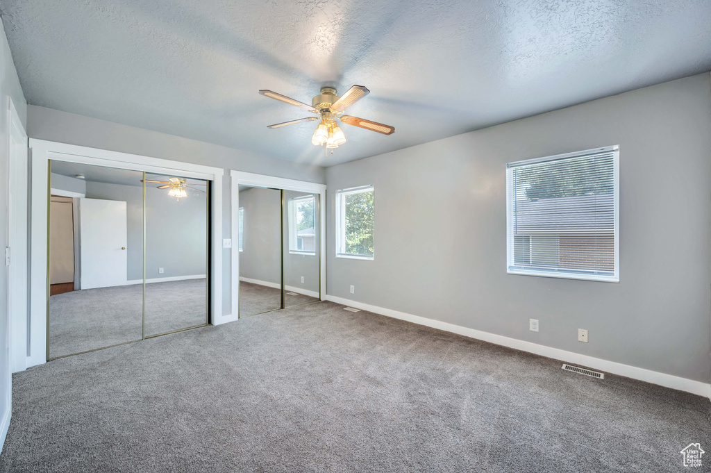Unfurnished bedroom featuring two closets, carpet, a textured ceiling, and a ceiling fan
