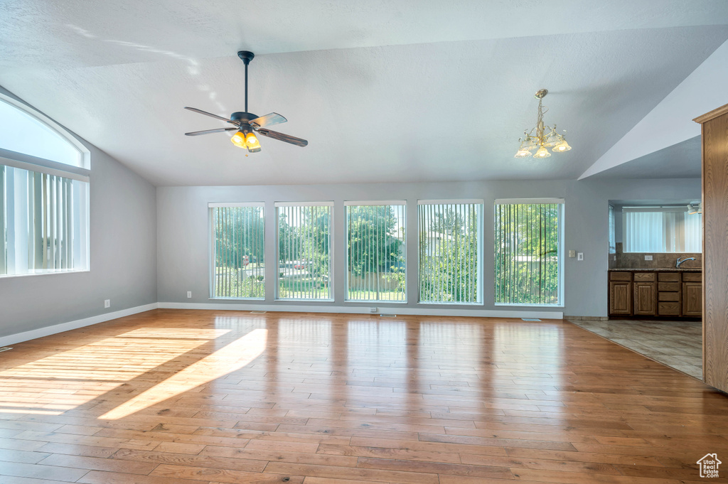Unfurnished living room with lofted ceiling, plenty of natural light, light wood-style flooring, and a chandelier