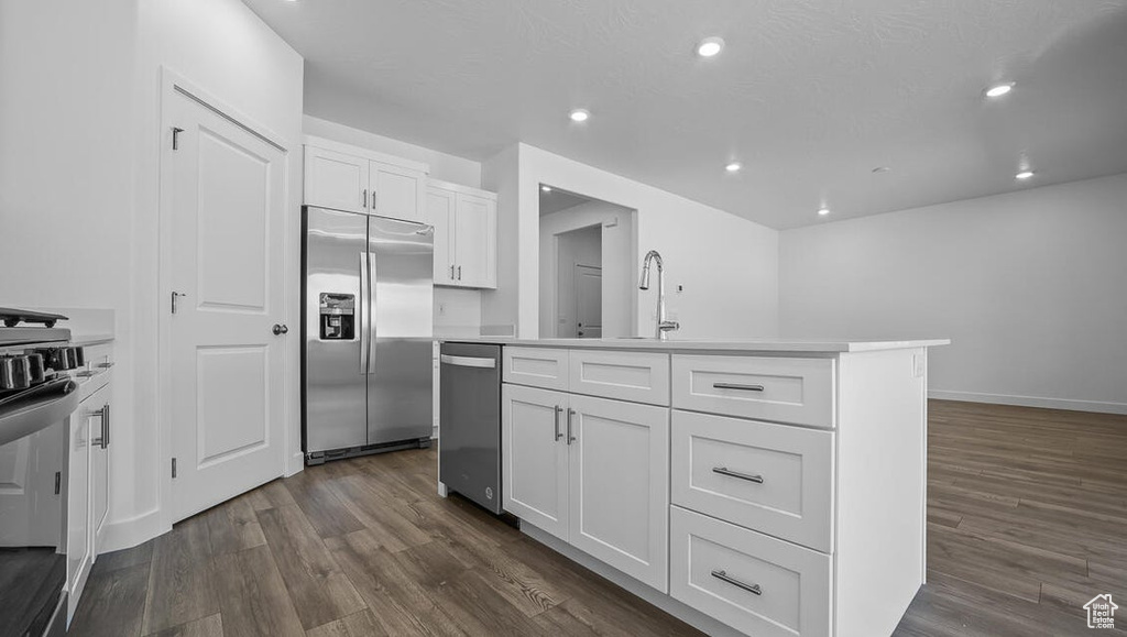Kitchen featuring stainless steel appliances, dark wood-style floors, white cabinets, an island with sink, and recessed lighting