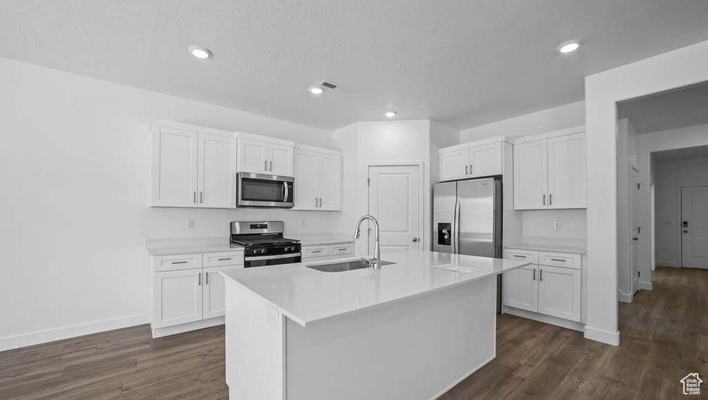 Kitchen with stainless steel appliances, dark wood-style flooring, white cabinets, a center island with sink, and recessed lighting