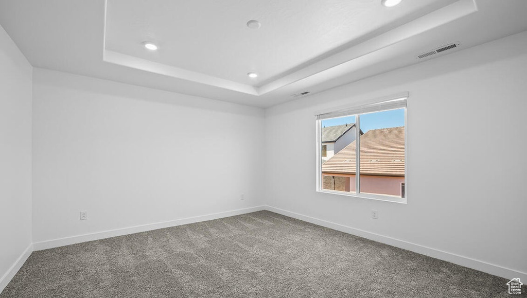 Empty room featuring a raised ceiling, carpet flooring, and recessed lighting