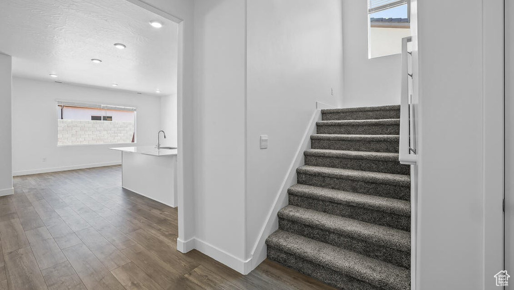 Staircase with healthy amount of natural light, wood finished floors, and recessed lighting