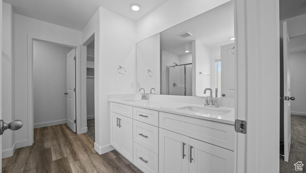 Full bath with a stall shower, double vanity, wood finished floors, and a walk in closet