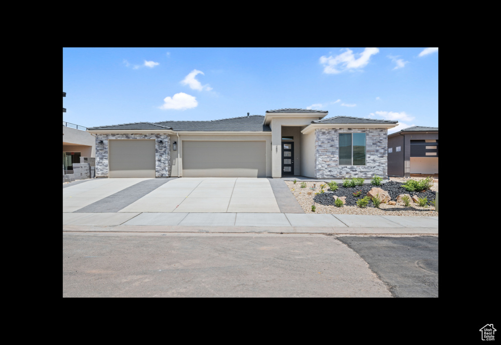 Prairie-style home with a garage, stone siding, stucco siding, driveway, and a tiled roof