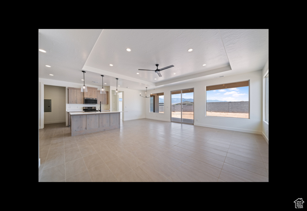 Unfurnished living room featuring a tray ceiling, ceiling fan, recessed lighting, and light tile patterned flooring