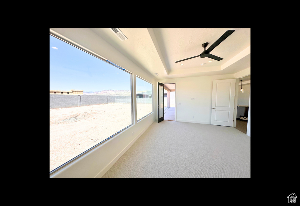 Empty room featuring ceiling fan, a raised ceiling, and light colored carpet