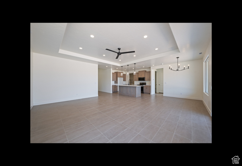 Unfurnished living room featuring a raised ceiling, a chandelier, ceiling fan, recessed lighting, and light tile patterned flooring