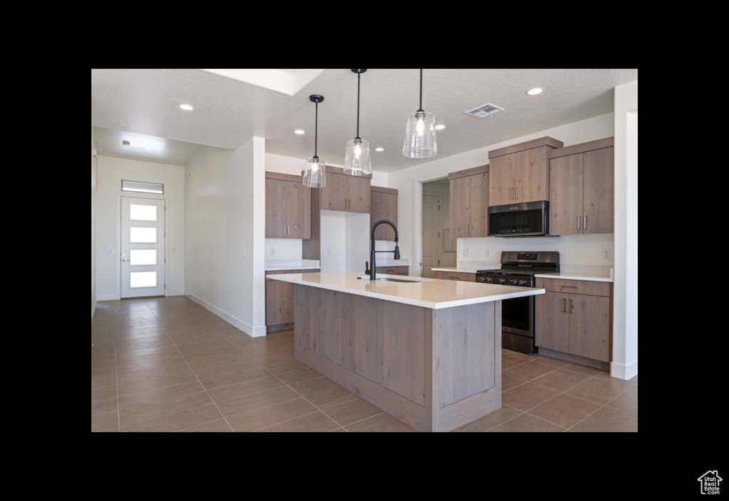 Kitchen featuring stainless steel appliances, light tile patterned floors, light countertops, a center island with sink, and recessed lighting