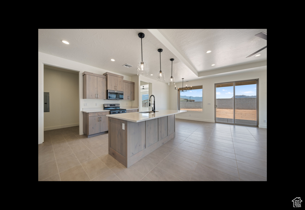 Kitchen with appliances with stainless steel finishes, a kitchen island with sink, light countertops, light tile patterned floors, and a chandelier