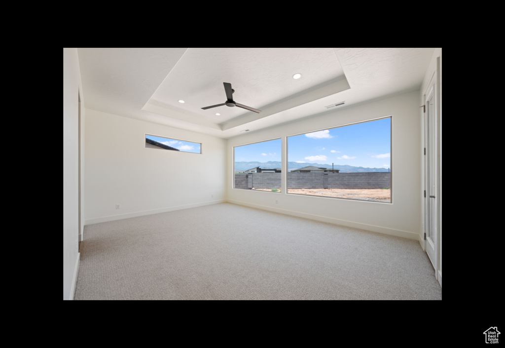 Carpeted spare room featuring a raised ceiling, a ceiling fan, and recessed lighting