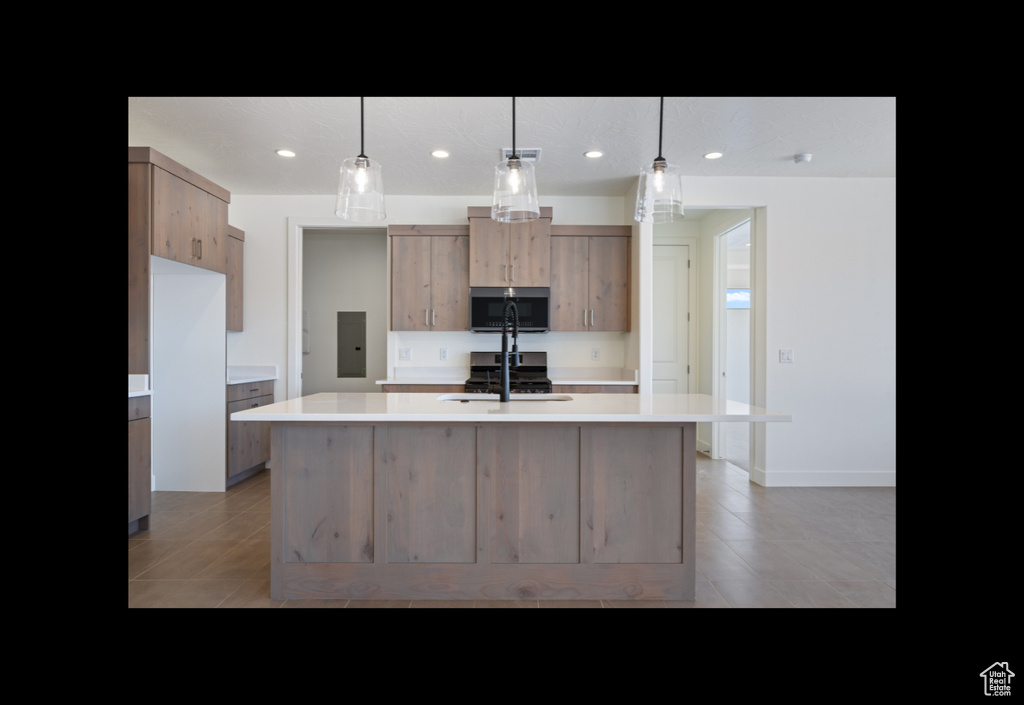 Kitchen featuring stainless steel microwave, light countertops, recessed lighting, an island with sink, and modern cabinets