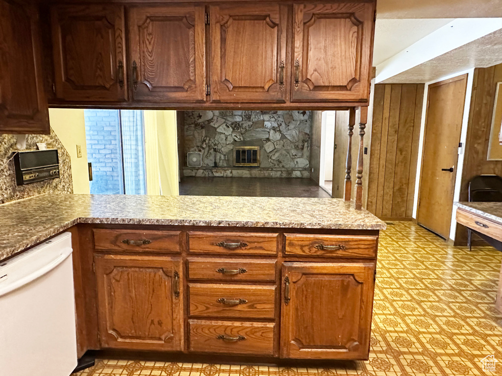Kitchen featuring white dishwasher, light flooring, backsplash, a fireplace, and brown cabinetry