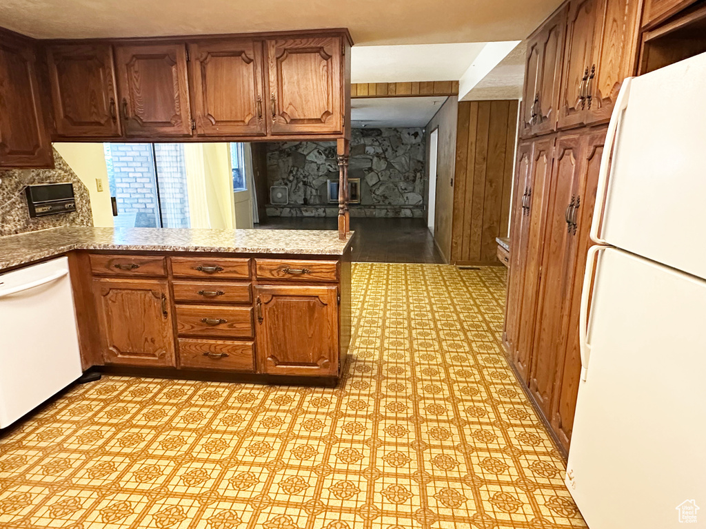 Kitchen featuring white appliances, light flooring, a peninsula, brown cabinets, and wooden walls