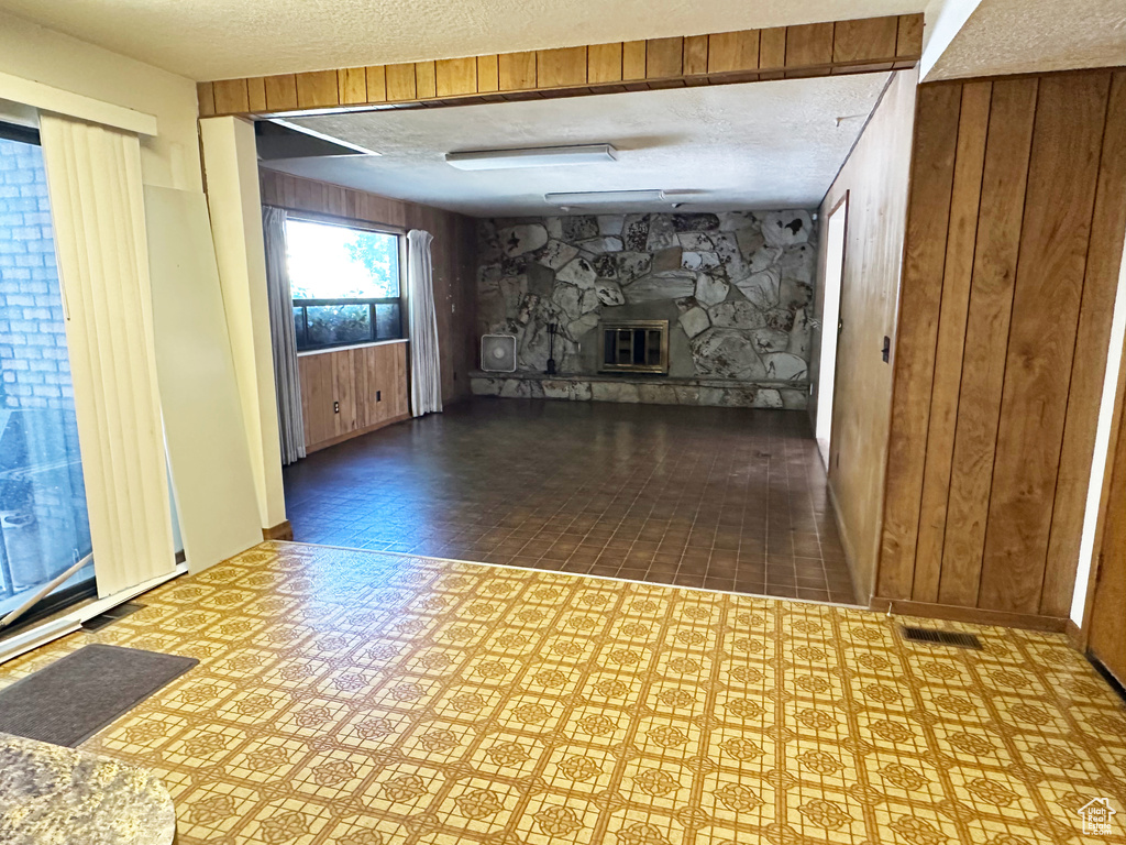 Unfurnished living room with wooden walls, a textured ceiling, a fireplace, and tile patterned floors