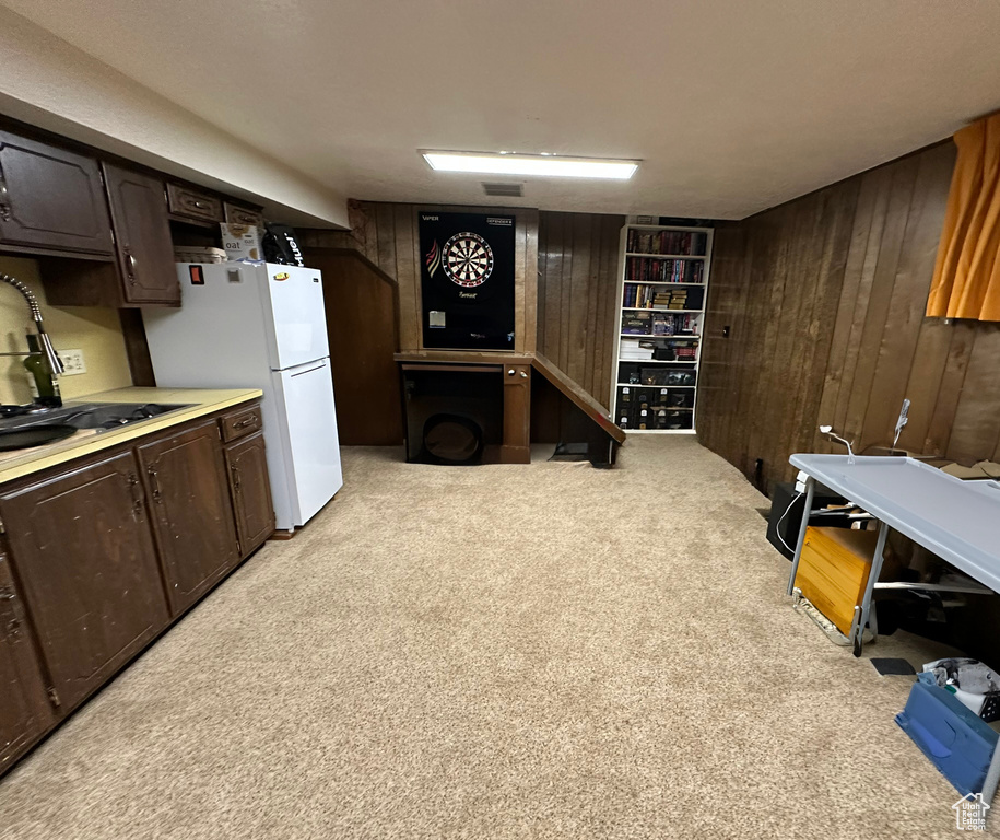 Interior space with wooden walls, light colored carpet, dark brown cabinetry, light countertops, and freestanding refrigerator