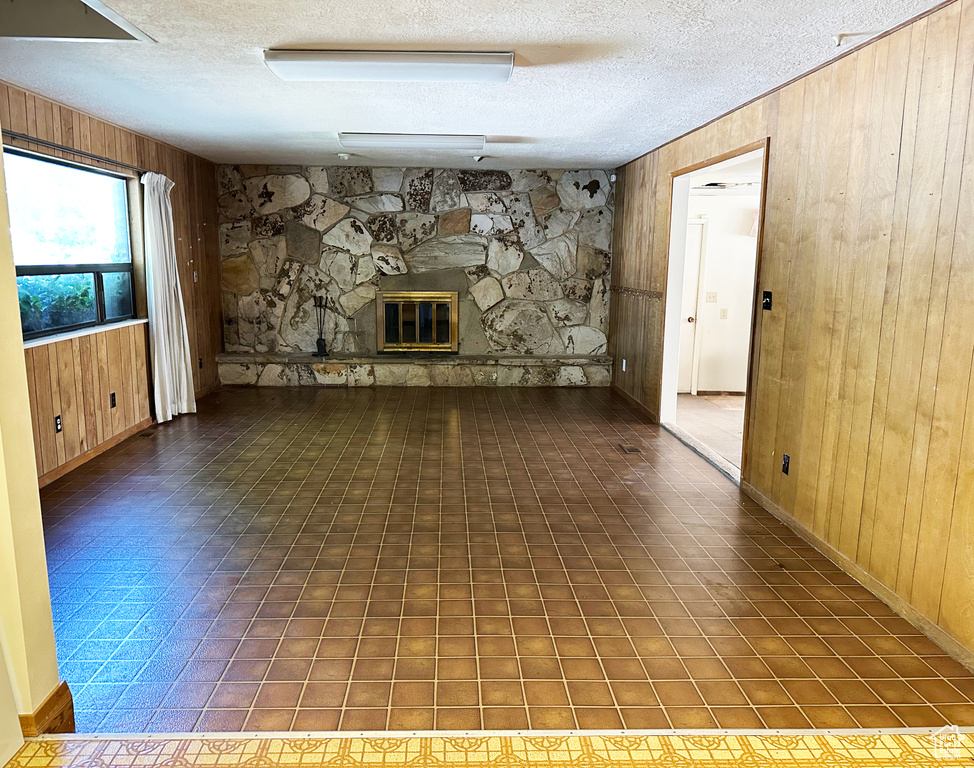 Unfurnished living room with wood walls, a textured ceiling, and a stone fireplace