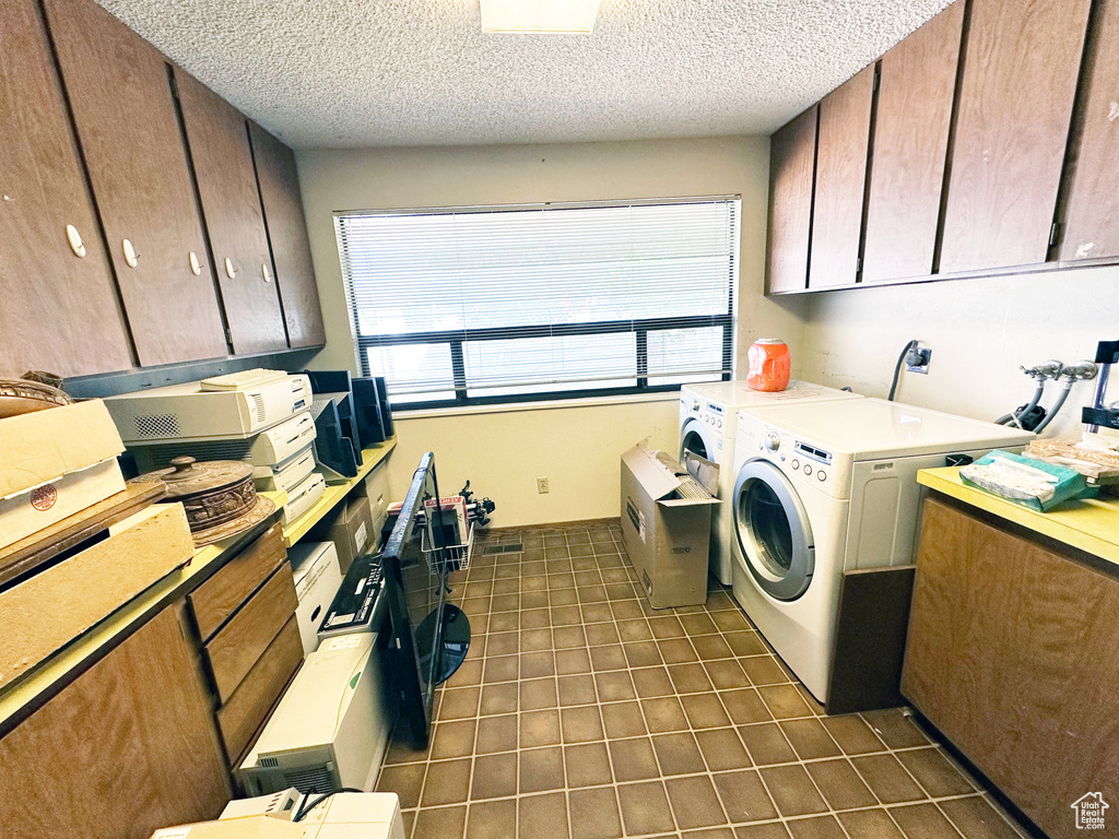 Washroom featuring washing machine and dryer, dark tile patterned floors, a textured ceiling, and cabinet space