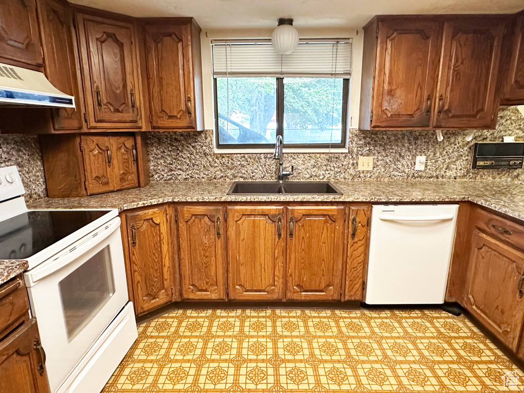 Kitchen featuring white appliances, under cabinet range hood, tasteful backsplash, and brown cabinets