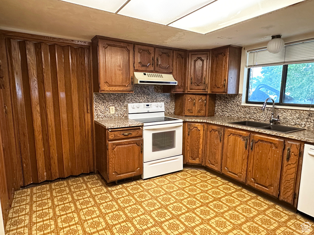 Kitchen with white appliances, under cabinet range hood, decorative backsplash, light flooring, and light countertops
