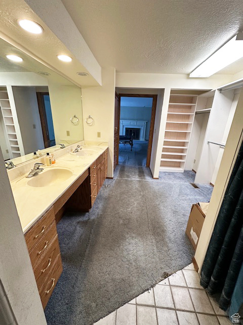 Bathroom with a textured ceiling, double vanity, built in shelves, a spacious closet, and recessed lighting