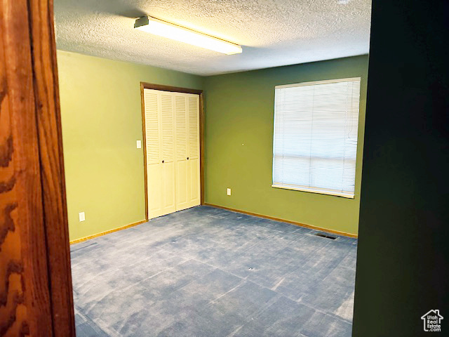 Unfurnished bedroom featuring dark colored carpet, a textured ceiling, and a closet