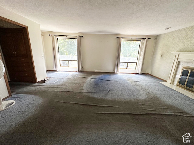 Unfurnished living room with carpet, a high end fireplace, and a textured ceiling