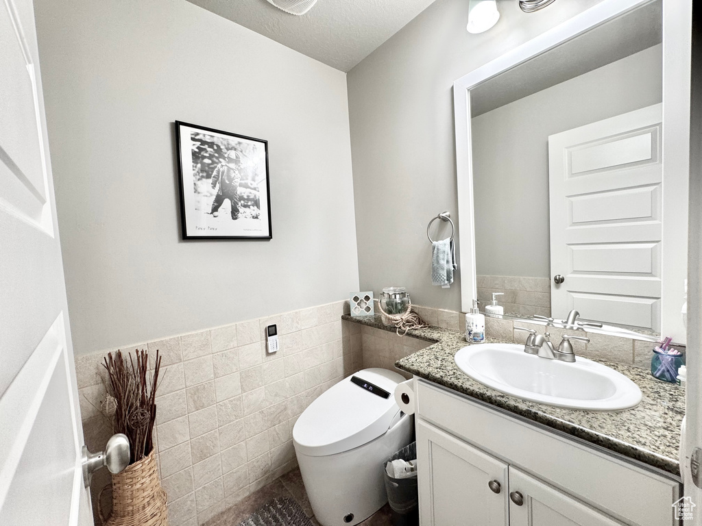 Bathroom featuring vanity, tile walls, a wainscoted wall, and a textured ceiling