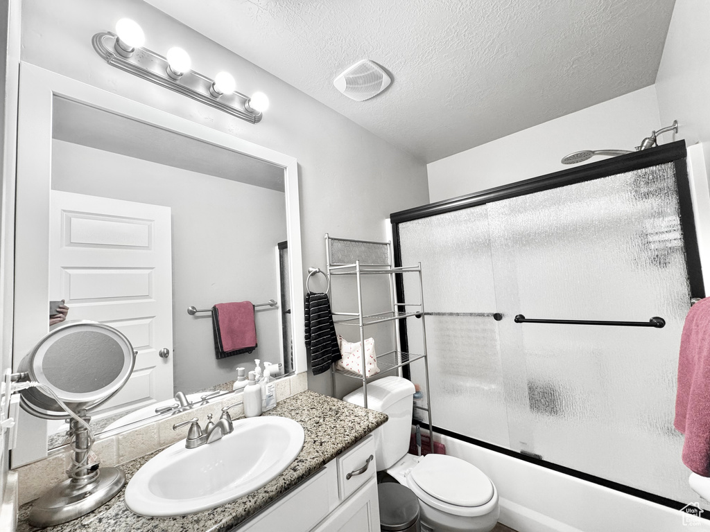Bathroom featuring vanity, combined bath / shower with glass door, and a textured ceiling