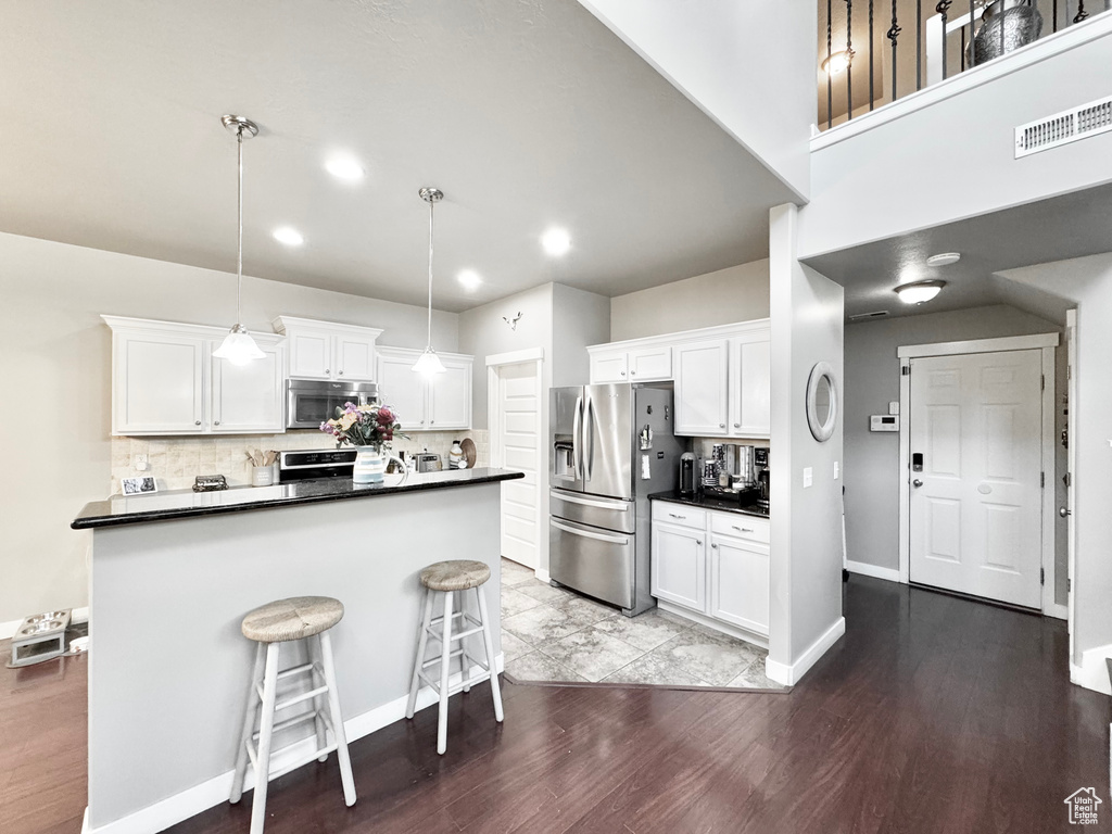 Kitchen with appliances with stainless steel finishes, white cabinets, dark countertops, wood finished floors, and recessed lighting