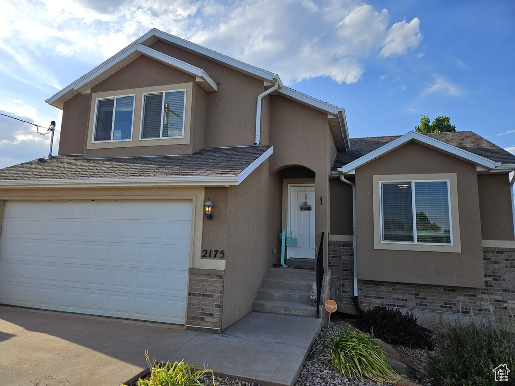 View of front facade with stucco siding, a garage, driveway, and roof with shingles
