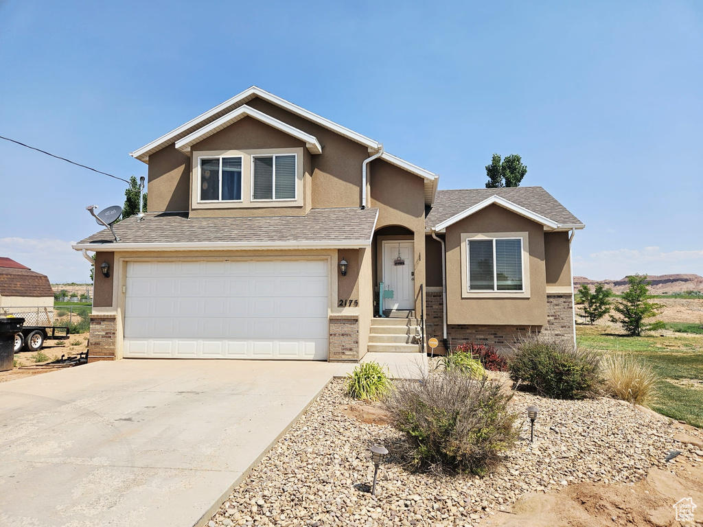 View of front of property featuring stucco siding, a garage, driveway, brick siding, and a shingled roof