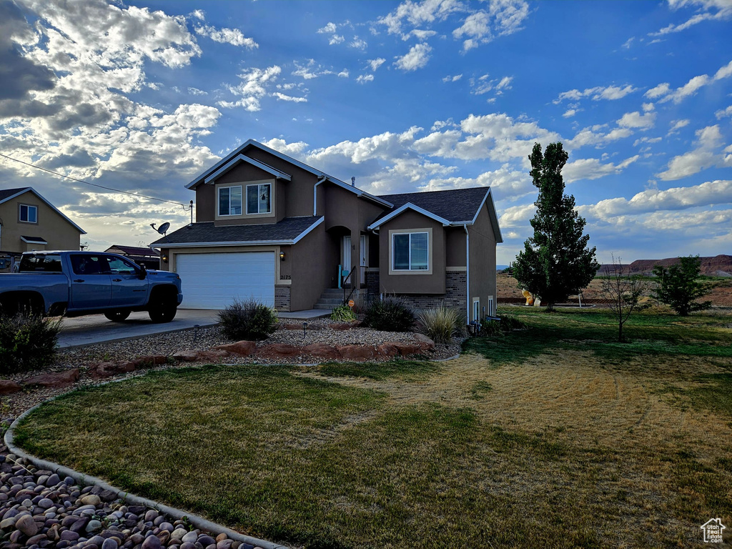 Traditional home featuring stucco siding, an attached garage, concrete driveway, and a front lawn