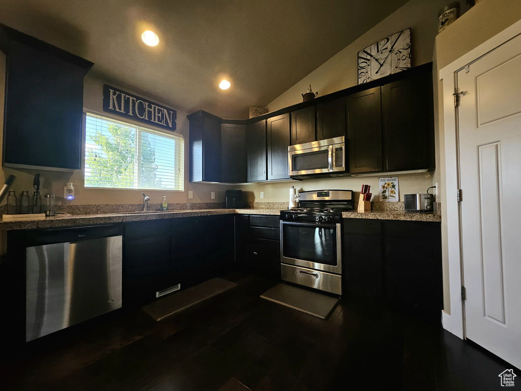 Kitchen with appliances with stainless steel finishes, dark cabinets, lofted ceiling, recessed lighting, and dark wood finished floors