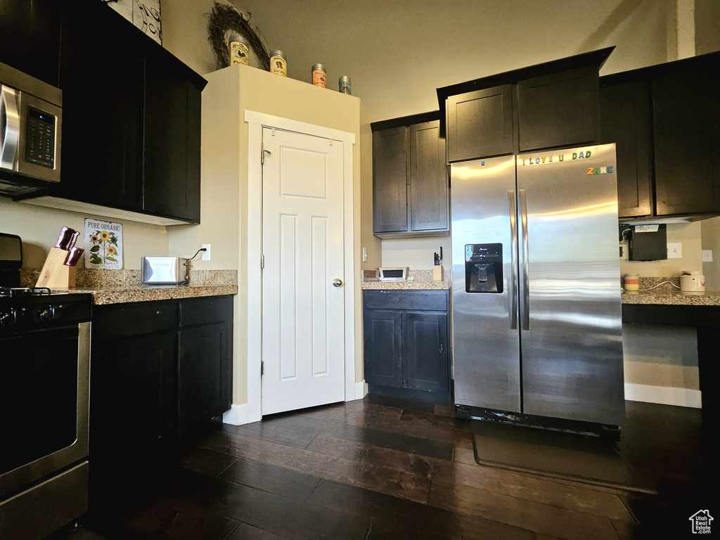 Kitchen featuring stainless steel appliances, dark wood-type flooring, and light stone countertops