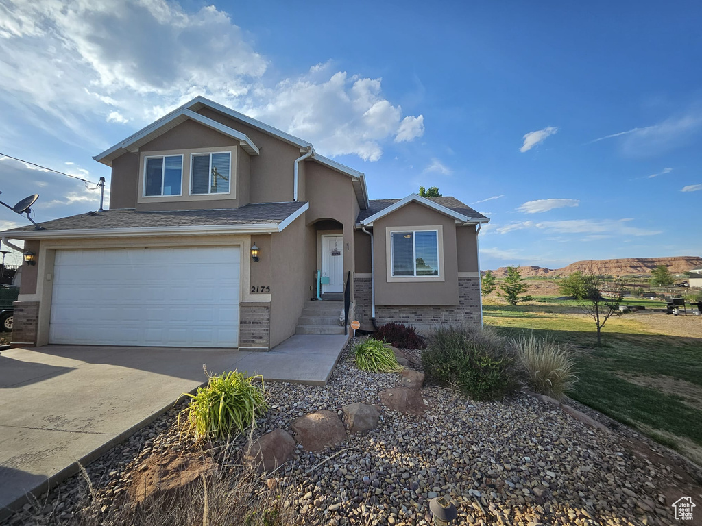 View of front of property with stucco siding, brick siding, a garage, and driveway